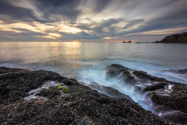 Günbatımında Güney Kaliforniya 'da huzurlu bir kaçış olan Crescent Bay Beach' te bulutlar gökyüzünü boyarken dalgalar yavaşça kayalık kıyılara çarpar..