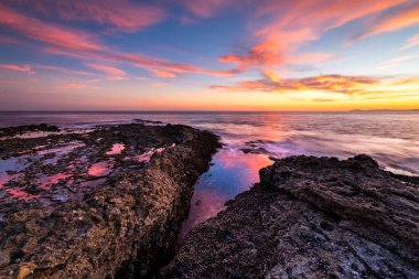 Güneş Laguna Beach, Orange County 'deki Crescent Bay Sahili' nde kayalık oluşumların ardında batarken gökyüzünü canlı renkler kaplıyor..