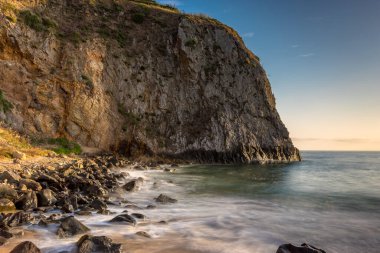 Dalgalar, Crystal Cove Sahili 'ndeki kayalık kıyılarda yavaşça dolaşarak Laguna Sahili, Kaliforniya' daki altın bir gökyüzünün altındaki büyüleyici uçurumları ortaya çıkarıyor..