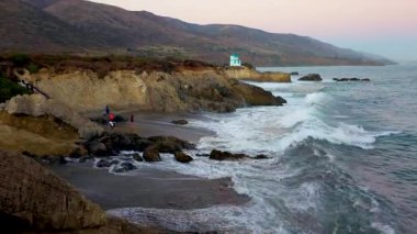 Leo Carrillo State Beach Malibu, California 'da engebeli uçurumları, huzurlu bir kıyı şeridini ve okyanus dalgalarını manzaralı günbatımında vurguluyor.