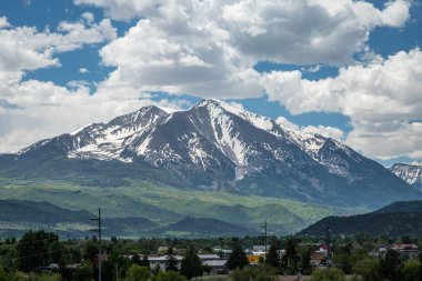 Colorado 'daki tüylü bulutlarla dolu mavi gökyüzünün altındaki yeşil vadilerin üzerindeki Sopris Dağı' nın görkemli karlı zirveleri..