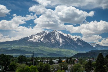 Colorado 'daki tüylü bulutlarla dolu mavi gökyüzünün altındaki yeşil vadilerin üzerindeki Sopris Dağı' nın görkemli karlı zirveleri..