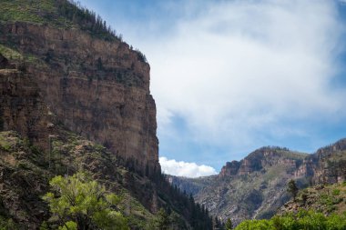 Glenwood Springs 'teki nefes kesici kanyon manzarası engebeli uçurumlar ve parlak mavi gökyüzünün altındaki canlı yeşillikler..