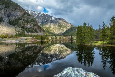 Subay Gulch Pond 'un berrak suları bulutlu gökyüzünün altında büyüleyici Rocky Dağları' nı yansıtıyor..