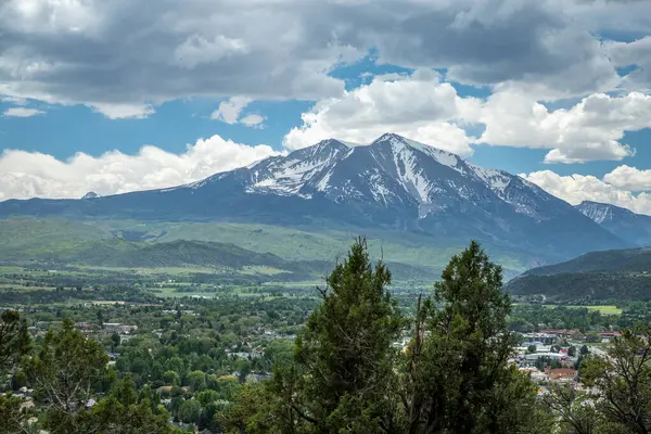 Colorado 'daki tüylü bulutlarla dolu mavi gökyüzünün altındaki yeşil vadilerin üzerindeki Sopris Dağı' nın görkemli karlı zirveleri..