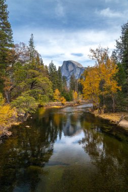 Half Dome uzaklardan yükselerek Yosemite Ulusal Parkı 'nda huzurlu ve manzaralı bir manzara oluştururken sonbahar renkleri sakin sulara yansıyor..