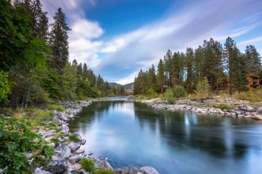 The tranquil Wenatchee River reflects the colorful sky at dusk, surrounded by lush forests and the majestic peaks of the Cascade Mountains. clipart