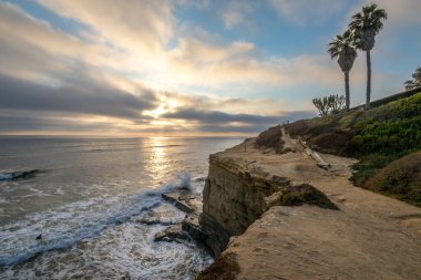 Point Loma 'nın kayalıklarında dinlendirici bir akşam. Güneş bulutların ardında batarken engebeli kıyıya vuran yumuşak dalgalarla..