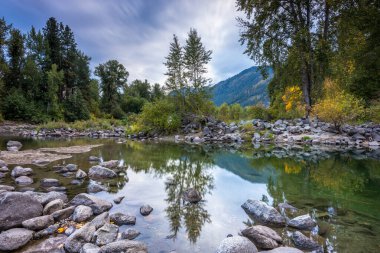 Colorful sunset casts a serene glow over the Wenatchee River, surrounded by lush greenery and vibrant mountains in Chelan County, Washington. clipart