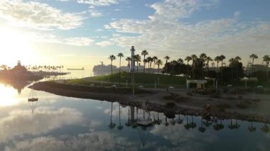 Lions Lighthouse ve Shoreline Aquatic Park 'ın gündoğumunda çekilen hava yörüngesi görüntüleri Long Beach, Kaliforniya' daki sakin suları ve uzak gemileri gösteriyor..
