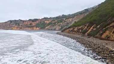 Bluff Cove, Palos Verdes Estates, Kaliforniya 'nın hava manzarası bulutlu bir günde sörfçülerin mükemmel dalgayı beklediği ve engebeli patika boyunca yürüyen insanların