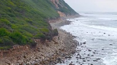 Sörfçüler bulutlu bir günde Kaliforniya, Palos Verdes Konutları 'nın engebeli sahillerinde yürüyorlar.