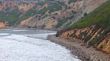 Sörfçüler bulutlu bir günde Kaliforniya, Palos Verdes Konutları 'nın engebeli sahillerinde yürüyorlar.