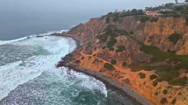 Kayalık sahil şeridi boyunca yürüyen sörfçülerle dolu bulutlu bir günde Palos Verdes Konutları 'nın dramatik Bluff Cove Trail' in hava görüntüleri.