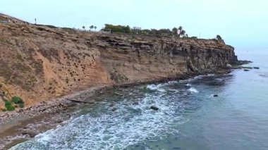 Los Angeles, Kaliforniya 'daki Point Fermin' in alçak hava manzarası, engebeli okyanus kayalıkları, çarpan dalgalar ve karamsar bulutlu kıyı manzarası