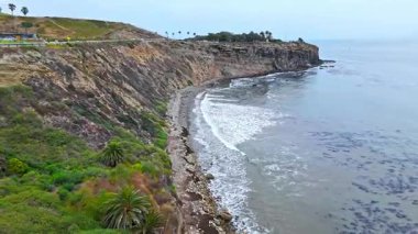 Los Angeles, Kaliforniya 'daki Point Fermin' in alçak hava manzarası, engebeli okyanus kayalıkları, çarpan dalgalar ve karamsar bulutlu kıyı manzarası
