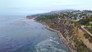 Los Angeles, Kaliforniya 'daki Point Fermin' in alçak hava manzarası, engebeli okyanus kayalıkları, çarpan dalgalar ve karamsar bulutlu kıyı manzarası