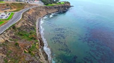 Los Angeles, Kaliforniya 'daki Point Fermin' in alçak hava manzarası, engebeli okyanus kayalıkları, çarpan dalgalar ve karamsar bulutlu kıyı manzarası