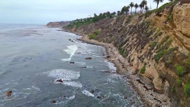 Los Angeles, Kaliforniya 'daki Point Fermin' in alçak hava manzarası, engebeli okyanus kayalıkları, çarpan dalgalar ve karamsar bulutlu kıyı manzarası