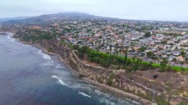 Los Angeles, Kaliforniya 'daki Point Fermin' in alçak hava manzarası, engebeli okyanus kayalıkları, çarpan dalgalar ve karamsar bulutlu kıyı manzarası