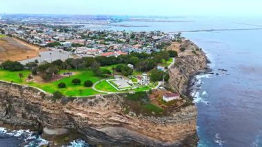 Los Angeles, Kaliforniya 'daki Point Fermin' in alçak hava manzarası, engebeli okyanus kayalıkları, çarpan dalgalar ve karamsar bulutlu kıyı manzarası