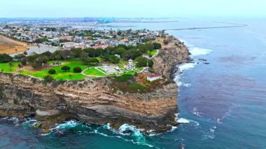 Los Angeles, Kaliforniya 'daki Point Fermin' in alçak hava manzarası, engebeli okyanus kayalıkları, çarpan dalgalar ve karamsar bulutlu kıyı manzarası