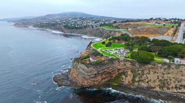 Los Angeles, Kaliforniya 'daki Point Fermin' in alçak hava manzarası, engebeli okyanus kayalıkları, çarpan dalgalar ve karamsar bulutlu kıyı manzarası