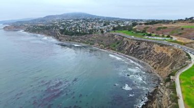 Los Angeles, Kaliforniya 'daki Point Fermin' in alçak hava manzarası, engebeli okyanus kayalıkları, çarpan dalgalar ve karamsar bulutlu kıyı manzarası