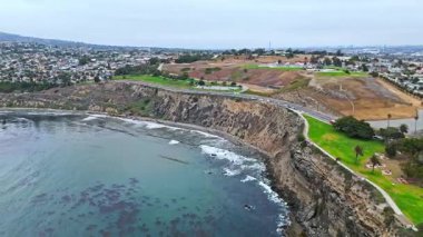 Los Angeles, Kaliforniya 'daki Point Fermin' in alçak hava manzarası, engebeli okyanus kayalıkları, çarpan dalgalar ve karamsar bulutlu kıyı manzarası