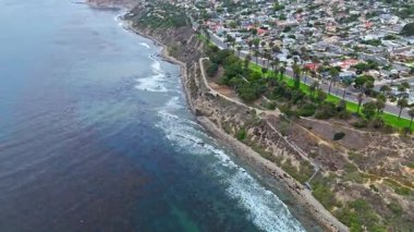 Los Angeles, Kaliforniya 'daki Point Fermin' in alçak hava manzarası, engebeli okyanus kayalıkları, çarpan dalgalar ve karamsar bulutlu kıyı manzarası