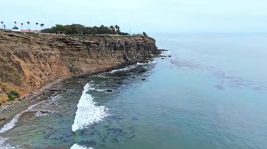 Los Angeles, Kaliforniya 'daki Point Fermin' in alçak hava manzarası, engebeli okyanus kayalıkları, çarpan dalgalar ve karamsar bulutlu kıyı manzarası