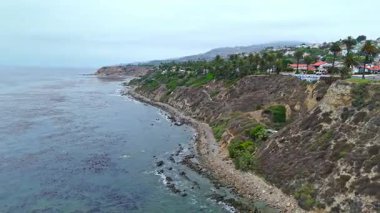 Los Angeles, Kaliforniya 'daki Point Fermin' in alçak hava manzarası, engebeli okyanus kayalıkları, çarpan dalgalar ve karamsar bulutlu kıyı manzarası