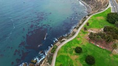 Los Angeles, Kaliforniya 'daki Point Fermin' in alçak hava manzarası, engebeli okyanus kayalıkları, çarpan dalgalar ve karamsar bulutlu kıyı manzarası