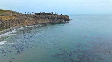 Los Angeles, Kaliforniya 'daki Point Fermin' in alçak hava manzarası, engebeli okyanus kayalıkları, çarpan dalgalar ve karamsar bulutlu kıyı manzarası