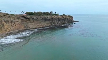 Los Angeles, Kaliforniya 'daki Point Fermin' in alçak hava manzarası, engebeli okyanus kayalıkları, çarpan dalgalar ve karamsar bulutlu kıyı manzarası