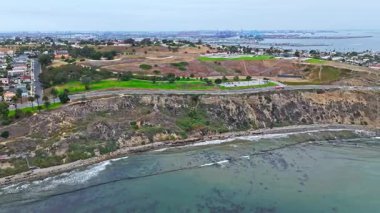 Los Angeles, Kaliforniya 'daki Point Fermin' in alçak hava manzarası, engebeli okyanus kayalıkları, çarpan dalgalar ve karamsar bulutlu kıyı manzarası