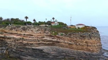 Los Angeles, Kaliforniya 'daki Point Fermin' in alçak hava manzarası, engebeli okyanus kayalıkları, çarpan dalgalar ve karamsar bulutlu kıyı manzarası