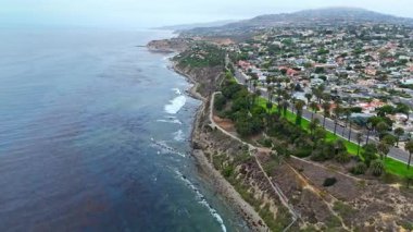 Los Angeles, Kaliforniya 'daki Point Fermin' in alçak hava manzarası, engebeli okyanus kayalıkları, çarpan dalgalar ve karamsar bulutlu kıyı manzarası