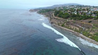 Los Angeles, Kaliforniya 'daki Point Fermin' in alçak hava manzarası, engebeli okyanus kayalıkları, çarpan dalgalar ve karamsar bulutlu kıyı manzarası