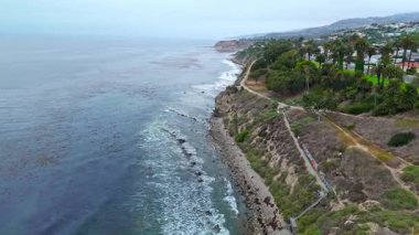 Los Angeles, Kaliforniya 'daki Point Fermin' in alçak hava manzarası, engebeli okyanus kayalıkları, çarpan dalgalar ve karamsar bulutlu kıyı manzarası