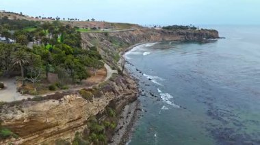 Los Angeles, Kaliforniya 'daki Point Fermin' in alçak hava manzarası, engebeli okyanus kayalıkları, çarpan dalgalar ve karamsar bulutlu kıyı manzarası