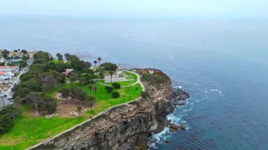 Los Angeles, Kaliforniya 'daki Point Fermin' in alçak hava manzarası, engebeli okyanus kayalıkları, çarpan dalgalar ve karamsar bulutlu kıyı manzarası