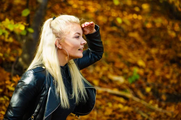 金发女人穿着时髦的衣服 在秋天的公园里 穿着黑色皮夹克的快乐女性与褐色叶子相映成趣 — 图库照片