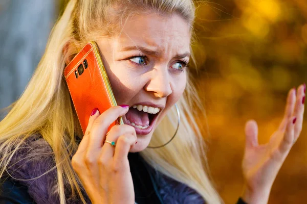 携帯電話を使用して 秋の公園を歩くブロンドの女性 怒っている女性はスマートフォンで話す — ストック写真