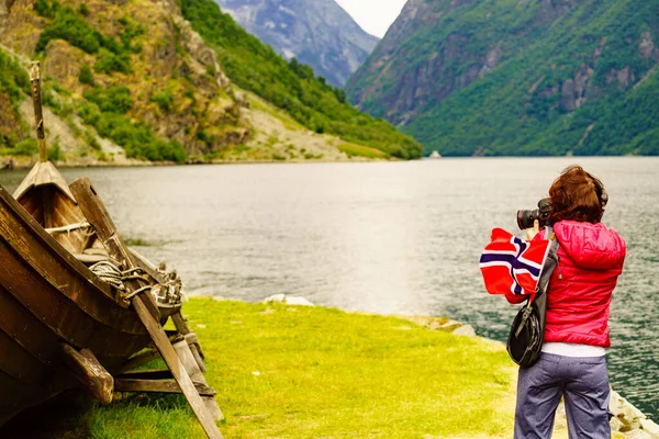 在峡湾岸边的老式木制维京船附近 女性游客带着挪威国旗 用相机拍照 旅游和旅行概念 — 图库照片