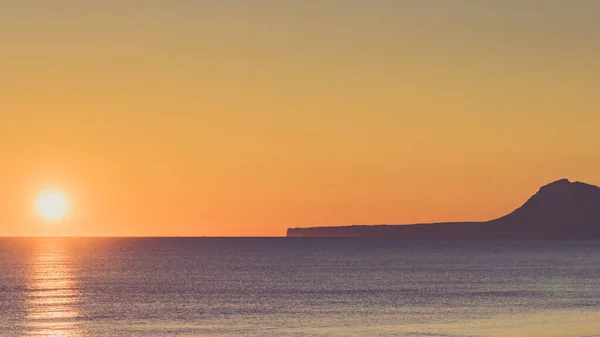 日出在海面上 从西班牙瓦伦西亚甘迪亚海滩看风景 蒙哥山地块轮廓呈现在地平线上 — 图库照片