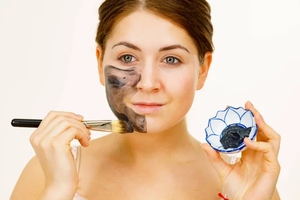 女人在她的脸上涂上黏土碳酸脱毒面罩 雌性用黑色化妆品和刷子托着碗 美容美发吓吓 — 图库照片