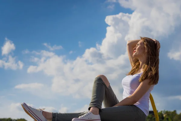 流行のファッショナブルな女性はカジュアルな履物の白いスニーカーと穴のズボンを着て屋外をリラックス 青い空に太陽の光を楽しむ女性 — ストック写真