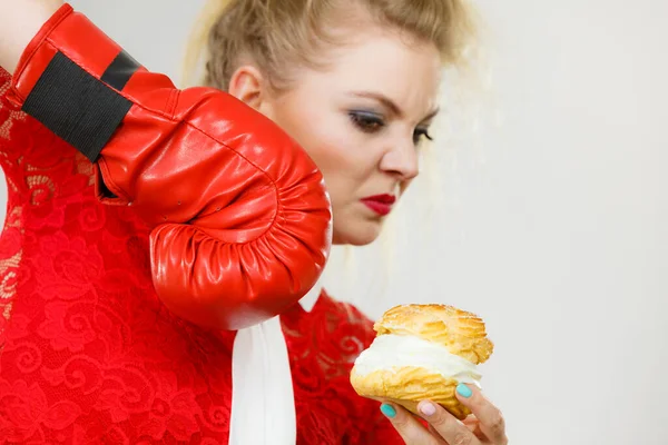 女性は ダイエットされている彼女の悪い習慣との戦い 女性の身に着けているボクシング グローブ持株甘いデザート クリーム ケーキ — ストック写真