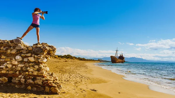 観光休暇や旅行 ビーチでの女性観光客のカメラで写真を撮る 背景に難破船 — ストック写真